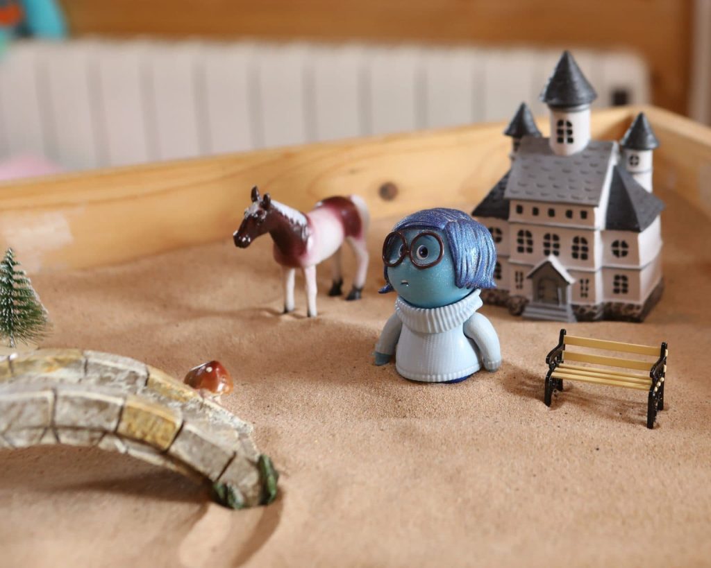 A colourful toy horse alongside a small toy house situated in a sandbox, inviting creative playtime for children