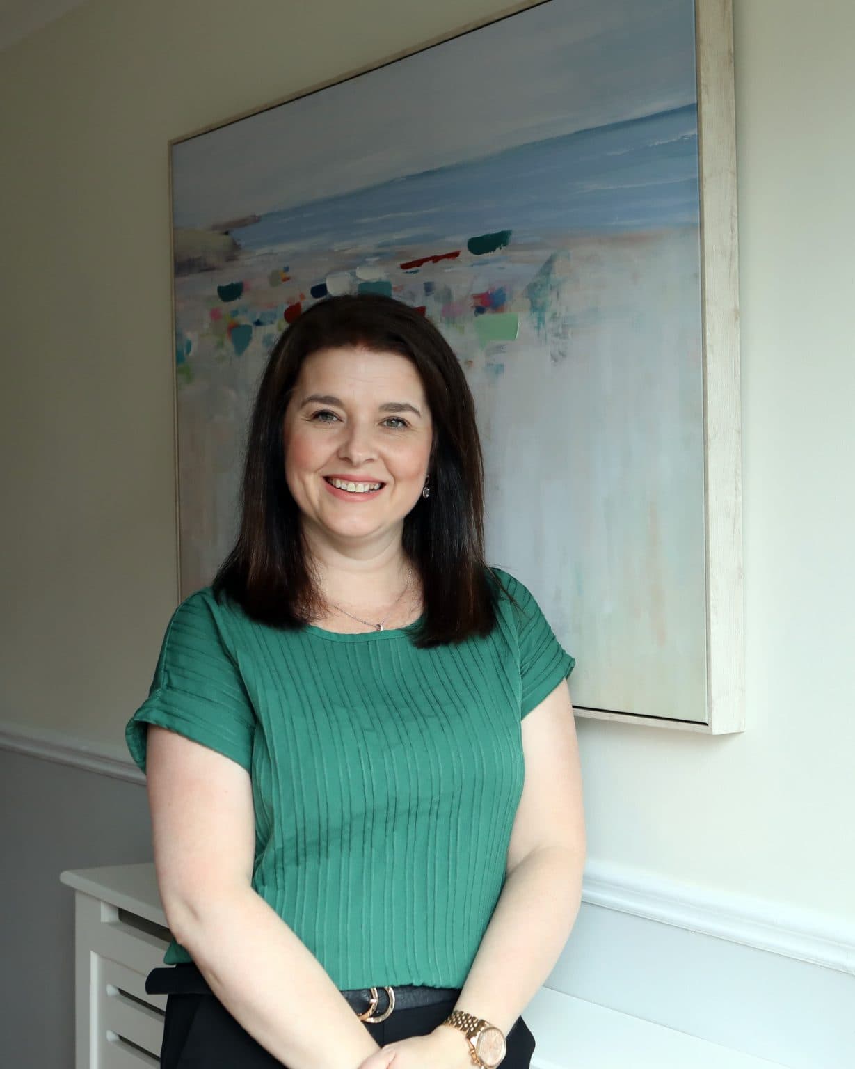 Melissa Moore, a woman wearing a green top stands in front of a colourful painting