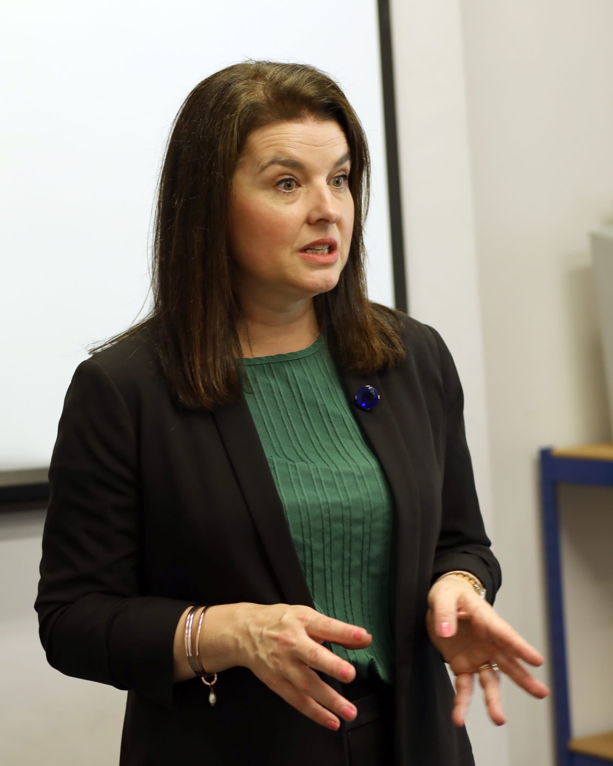 Melissa Moore, a woman in a green shirt and black jacket is conversing, reflecting an engaging and professional interaction.