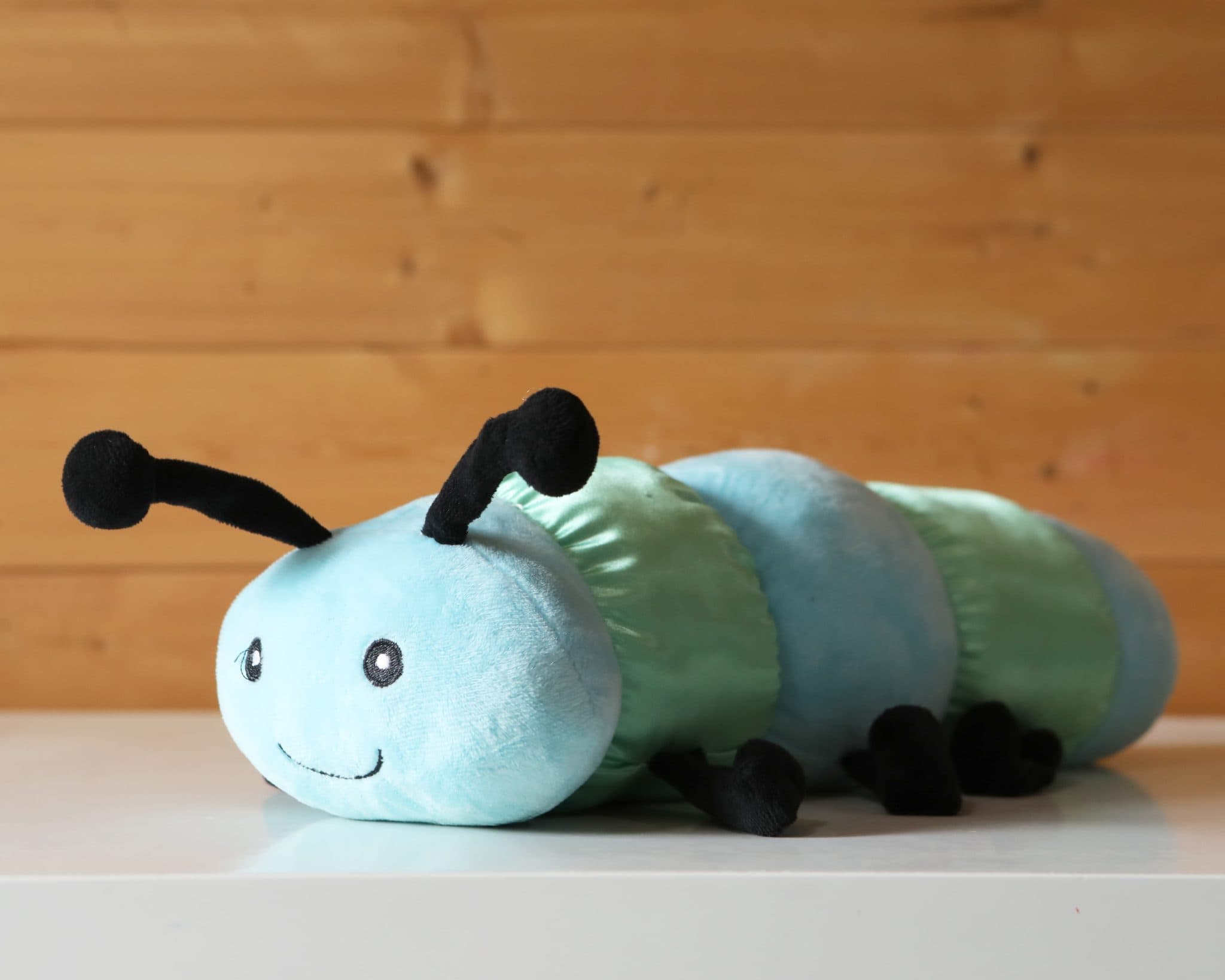 The Calming Caterpillar -a colourful stuffed caterpillar resting on a wooden table, showcasing its plush texture and vibrant design.